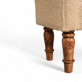 Close-up of the carved wooden leg of the beige upholstered bench, showcasing its intricate design.