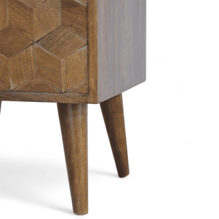 Close-up of angled side panel on geometric wood nightstand, highlighting smooth chestnut finish and cube-inspired carvings