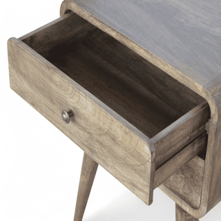 Open drawer of a grey-washed nightstand revealing spacious storage with a wooden finish.