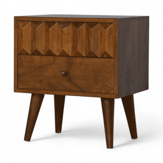 Angled front view of mango wood nightstand showcasing carved prism details on the top drawer, smooth chestnut finish, and tapered legs